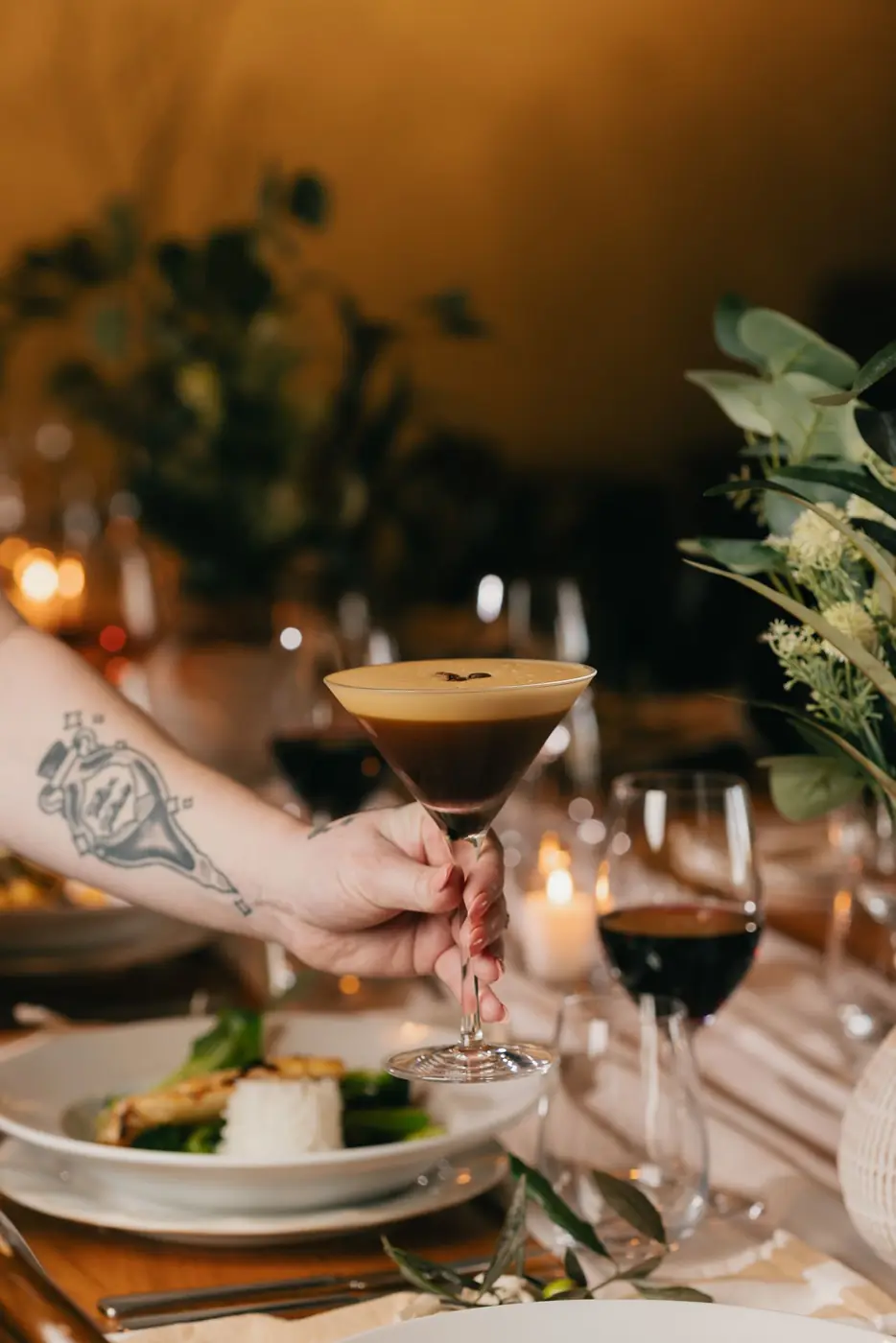 An espresso martini and a plate at a candlelit dinner table