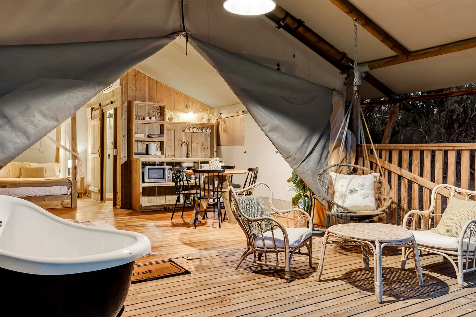 A safari tent at dusk with its deck, outdoor bath and egg chair
