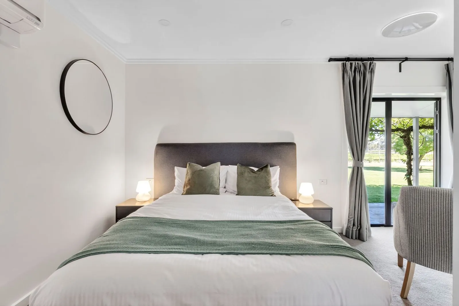 A queen bed with green cushions and bedside lamps, glass doors open to the vineyard